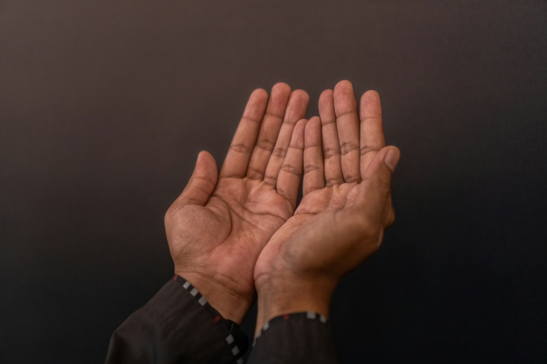 Two hands cupped open in dua against a dark background