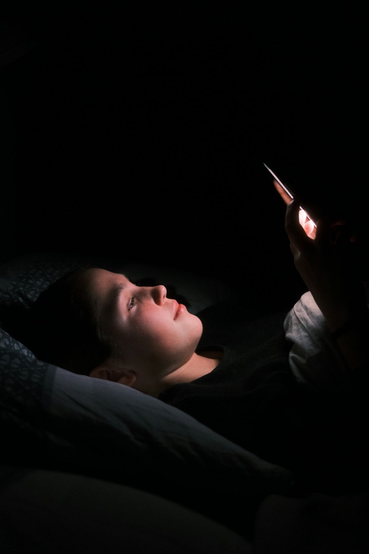 A person lying in bed in the dark, lit only by a phone screen