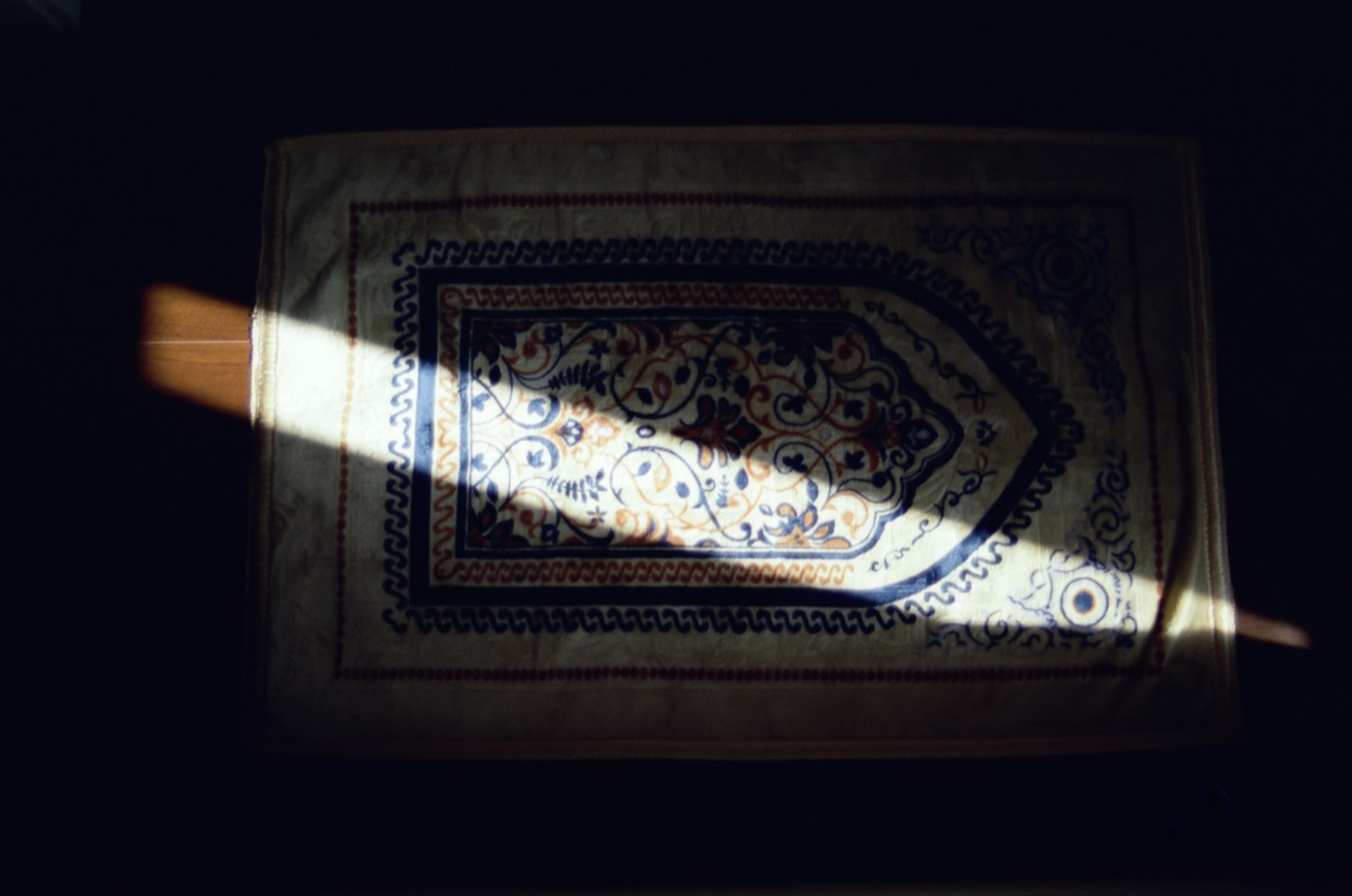 A prayer mat on a dark floor, crossed by a single shaft of light